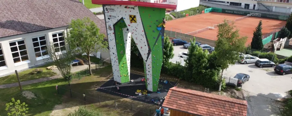 Aerial view of the tower beside the school sports hall, with a climber high on the green wall