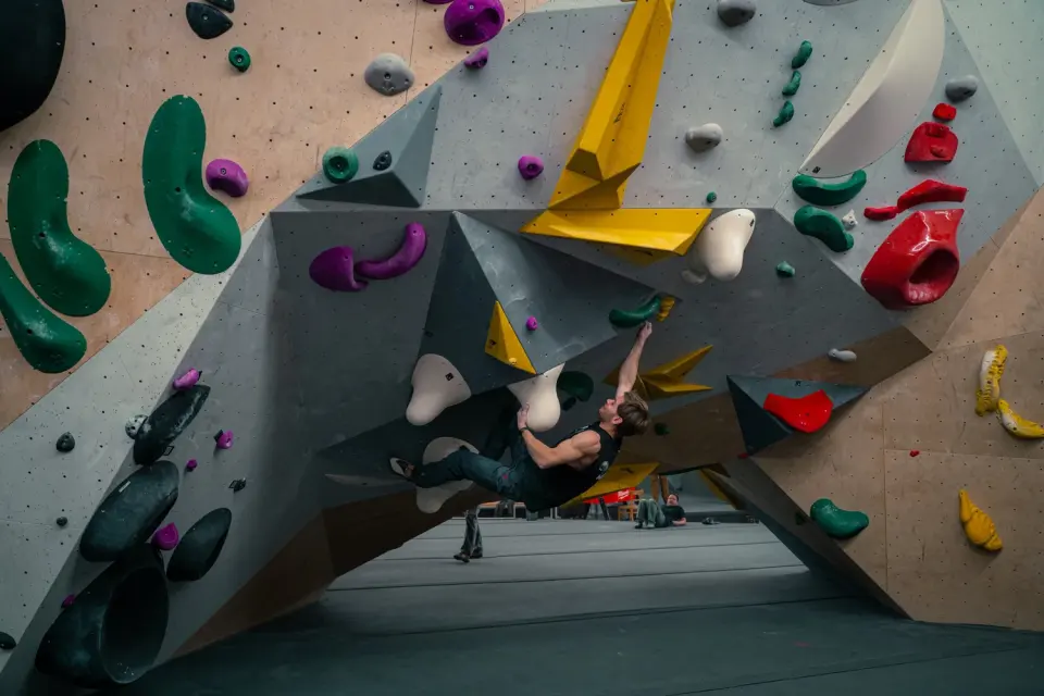 Climber on a steep boulder problem with grey volumes and colourful holds at Newton Kapfenberg