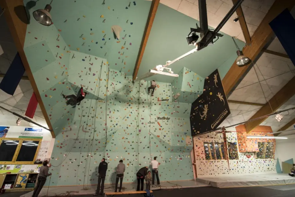 Climbers and belayers at the green lead wall, with the bouldering wall to the right