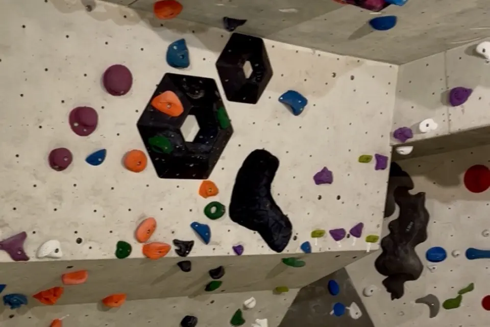 Grey bouldering walls with coloured holds and black hexagonal volumes below an overhang