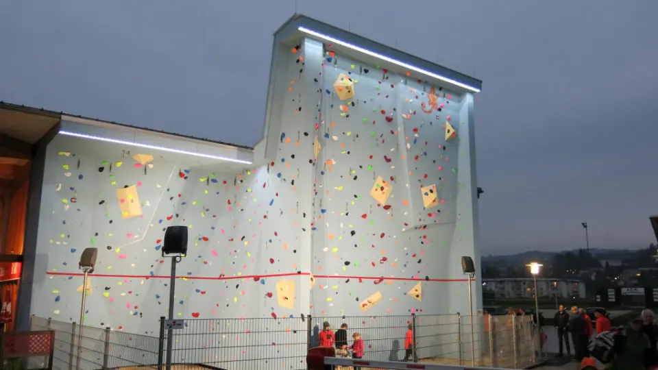 Floodlit outdoor climbing wall beside the sports park building at dusk
