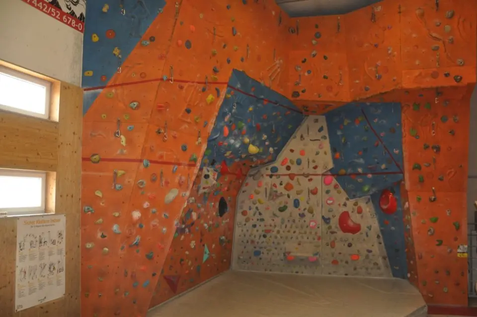 Orange and blue lead wall with quickdraws above a matted boulder corner