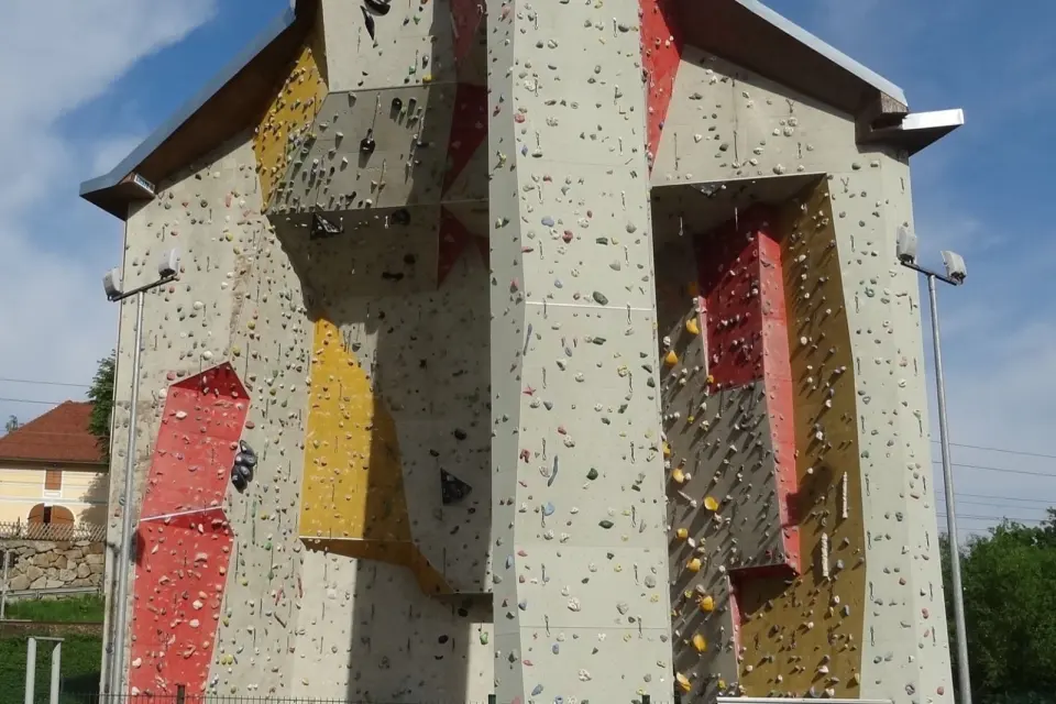 Outdoor climbing tower with grey, red and yellow walls and floodlights behind a fence