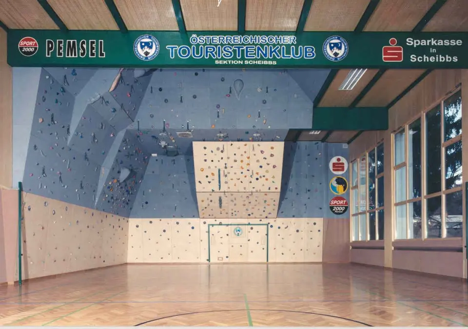 Blue and wooden climbing walls with overhangs at the end of a school sports hall