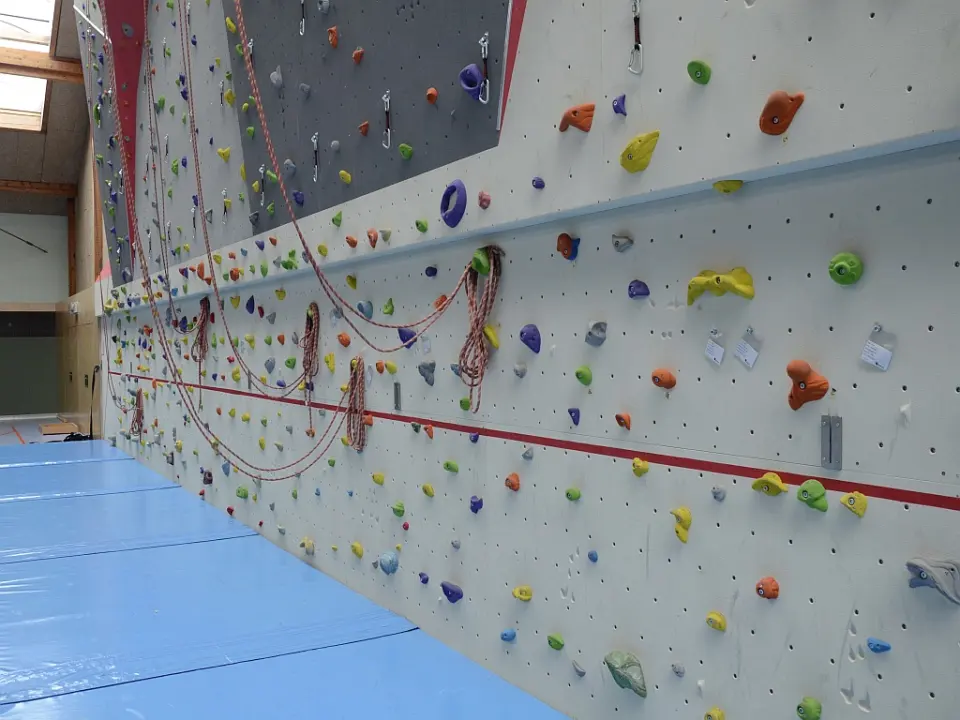 Ropes coiled along the foot of the climbing wall above blue floor mats