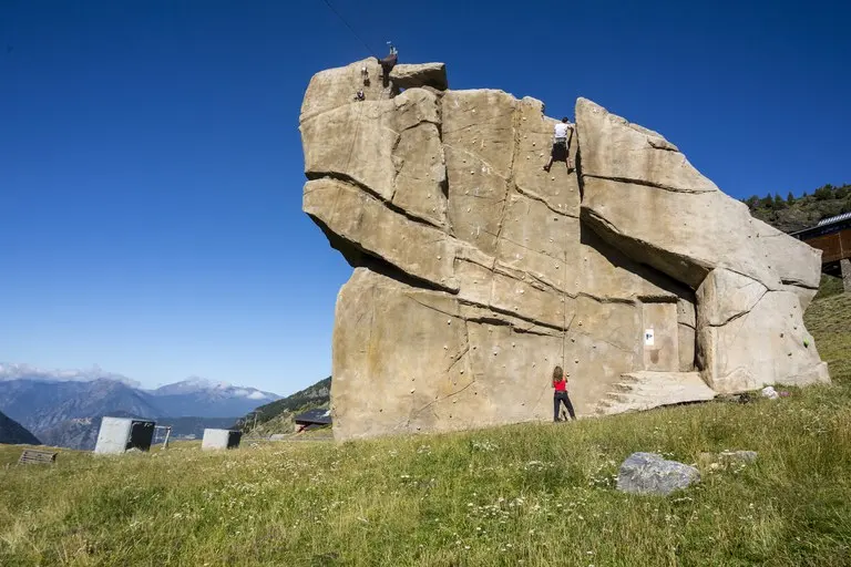 Climbers on the broad face of the outdoor wall, with mountains behind