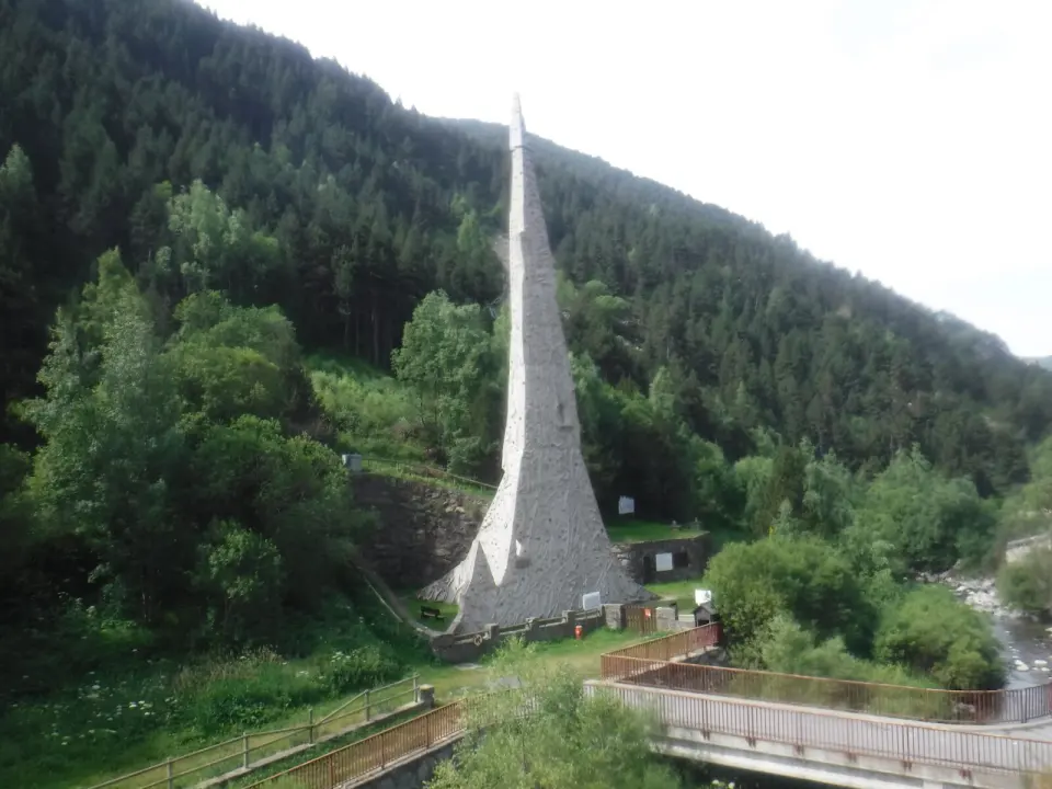 Tapering 33-metre outdoor climbing spire beside the river, with wooded hillside behind
