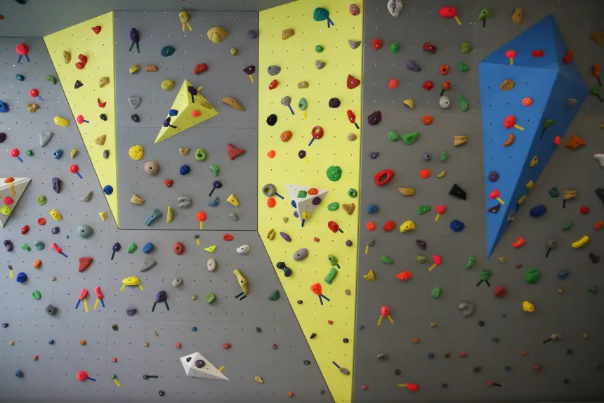 Grey and yellow bouldering wall with triangular volumes and a large blue volume