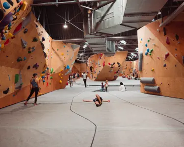 Bouldering hall with orange walls, grey matting and ducts under the warehouse roof