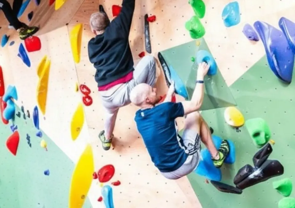 Climbers on plywood and green walls set with colourful holds and volumes