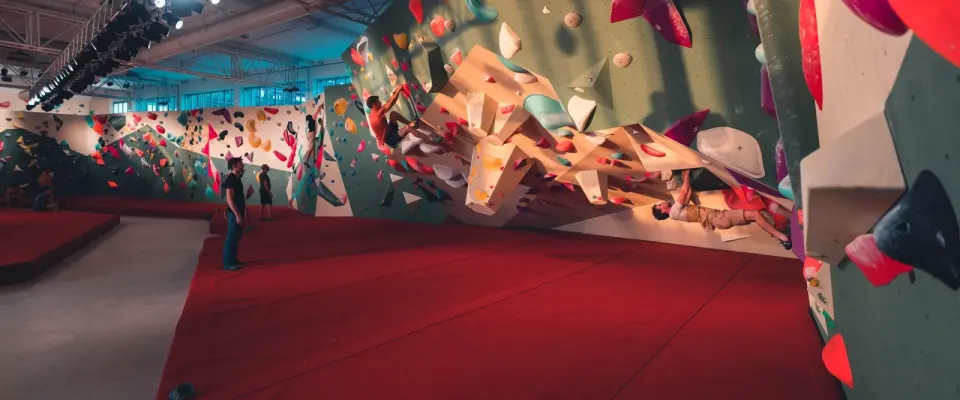 Climbers on the long bouldering wall above red matting in the high hall