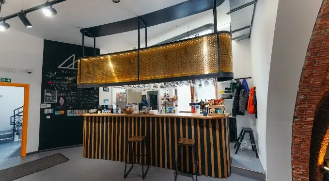 Bar with a slatted wooden counter and stools under a gold metal canopy