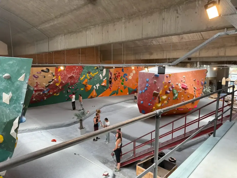 The bouldering hall seen from the mezzanine, with long walls and a freestanding boulder