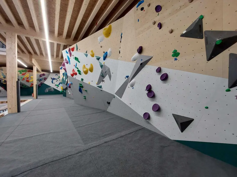 Bouldering wall under a timber-beamed ceiling, with grey matting below