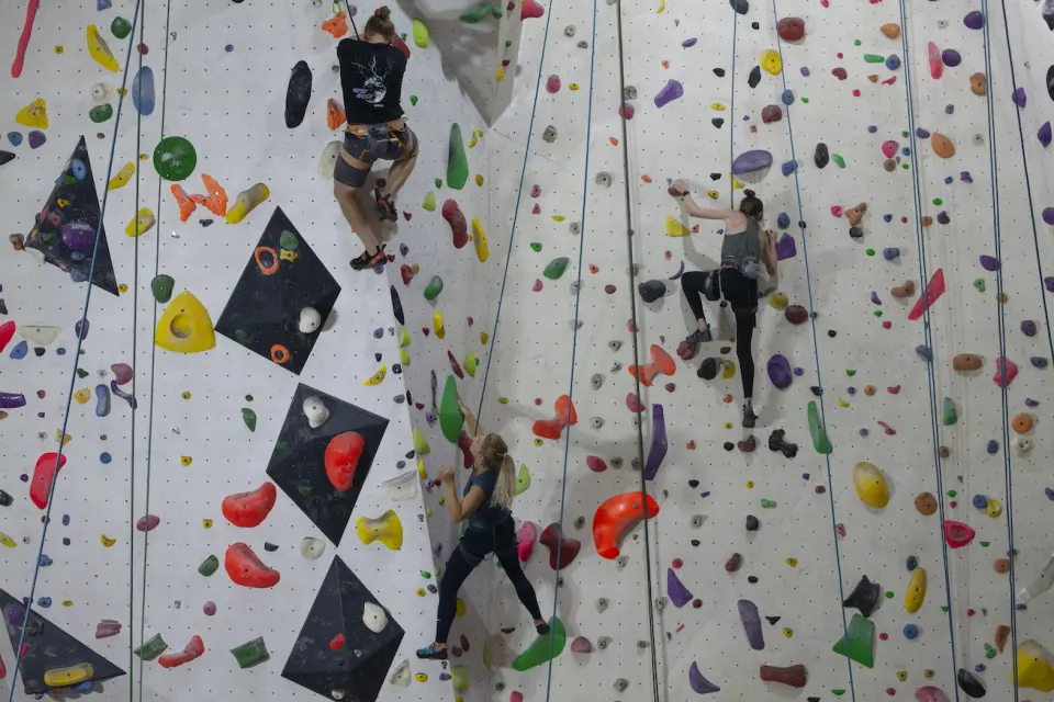 Three climbers on top ropes on the tall white walls