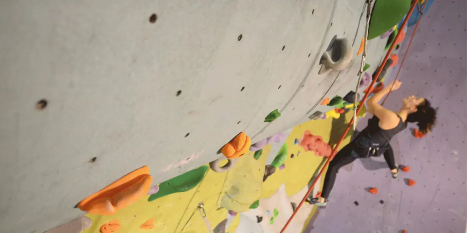 Climber on a rope below a grey overhang, with yellow and purple walls behind
