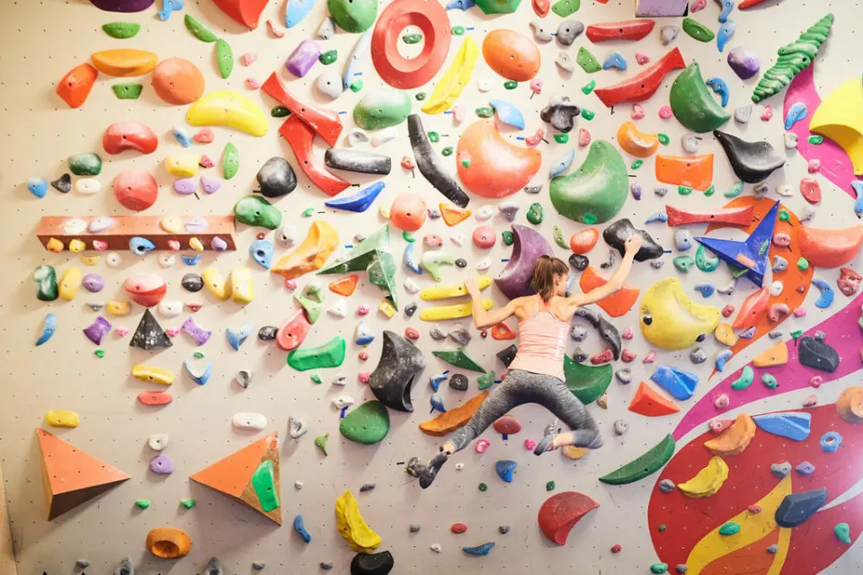 Climber reaching across a bouldering wall packed with brightly coloured holds