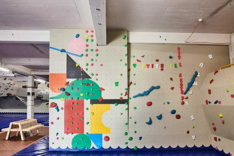 Painted bouldering wall spelling out Petite Ile in holds, above blue matting