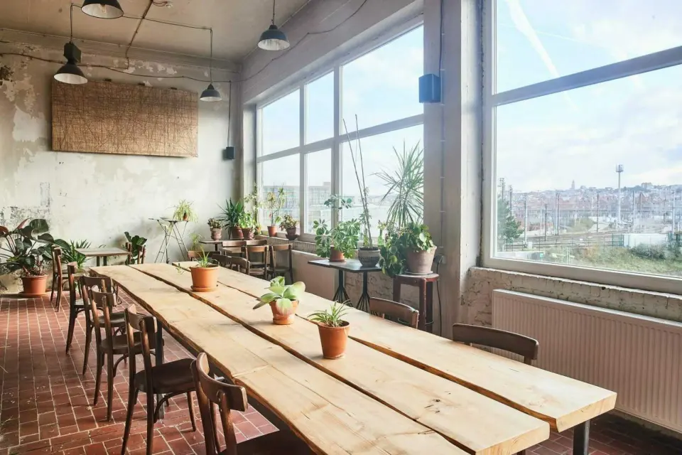 Long wooden table and plants by tall windows looking over the railway and the city