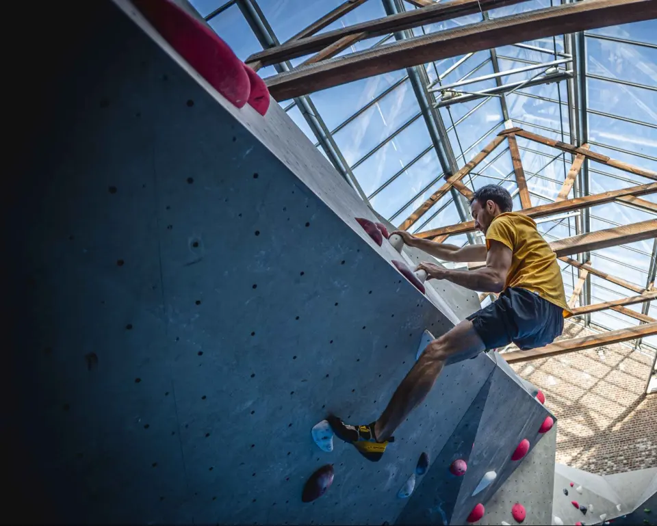 Climber on a steep boulder beneath the hall's glass roof and timber beams