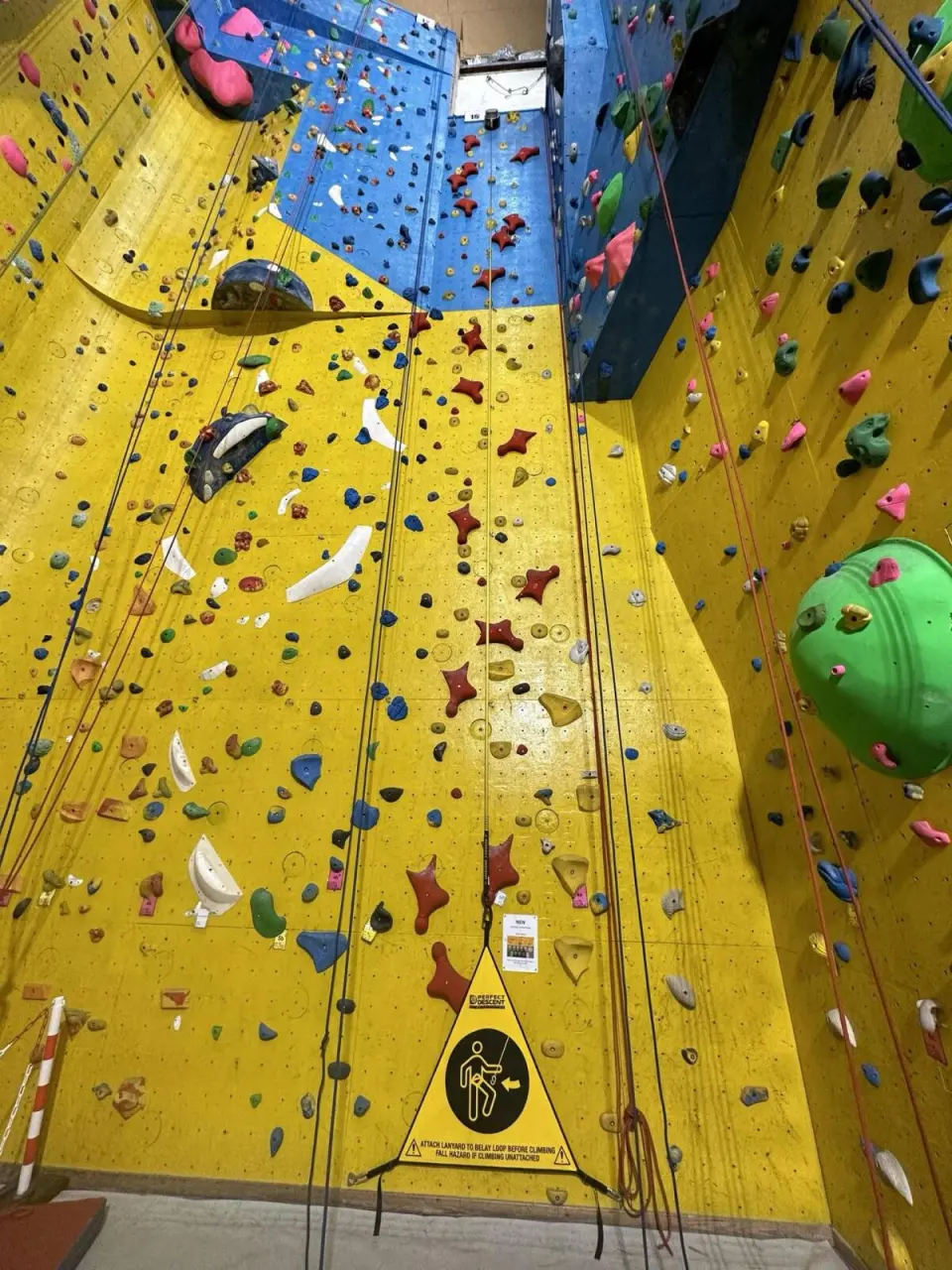 Auto-belay at the foot of a tall yellow wall, with a blue headwall above