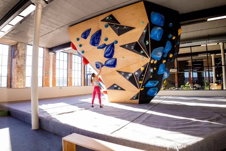 Climber at a freestanding plywood boulder below the mill's tall windows and iron columns