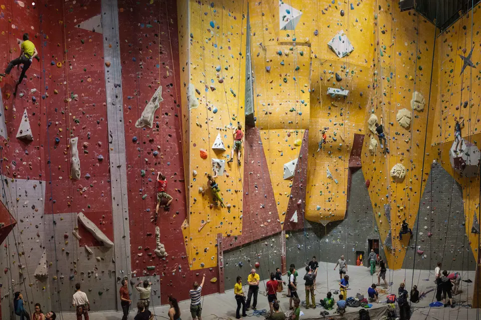 Climbers on the red and yellow walls of the indoor rope hall, with belayers below
