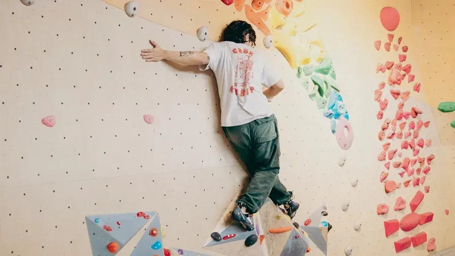 Climber on a vertical wall with colourful holds and triangular volumes