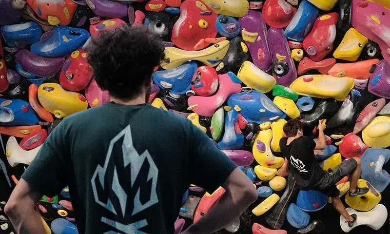 Spray wall covered in holds, with one climber on it and another watching