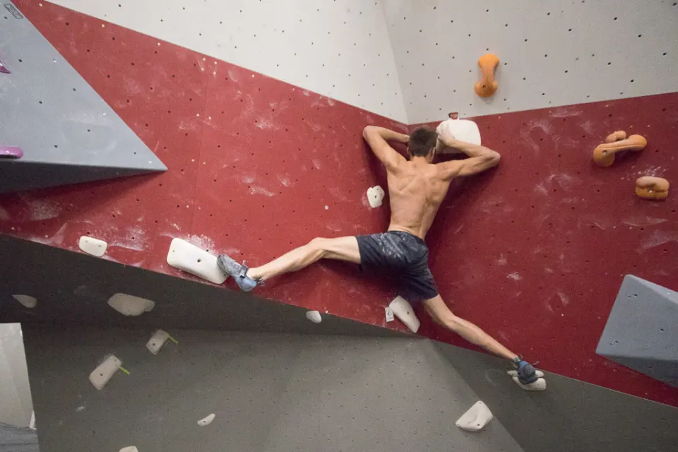 Climber bridging wide across a red corner with volumes and big holds