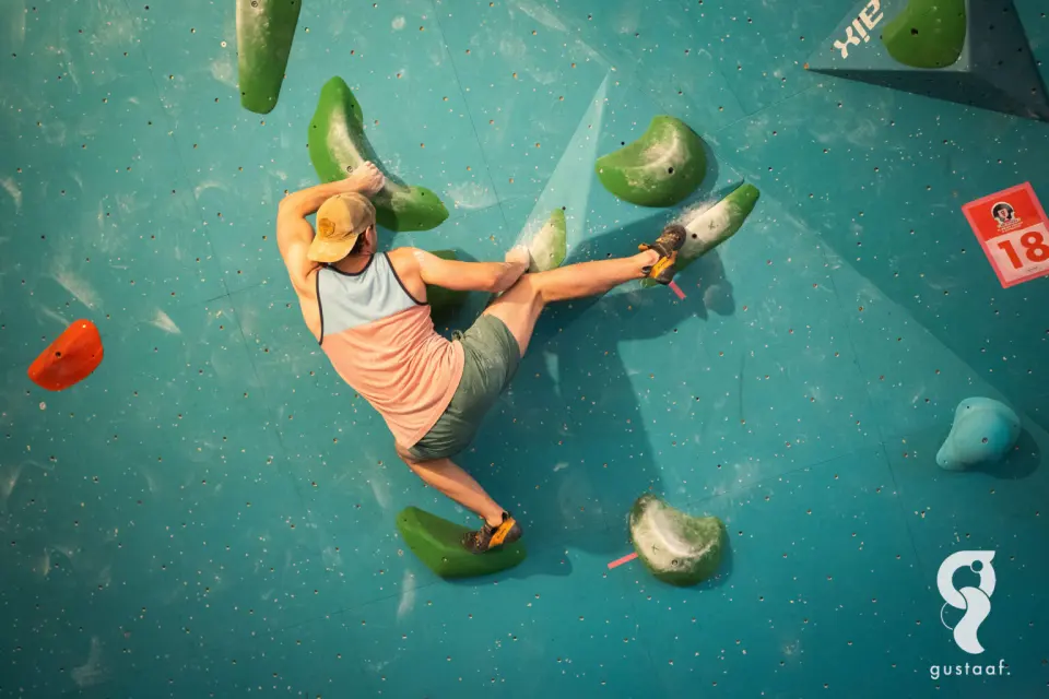 Climber high-stepping between green holds on a teal wall during the Art Niveau competition