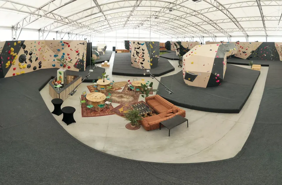 Panorama of the bouldering hall under a white tent roof, with freestanding boulders and a lounge with sofas