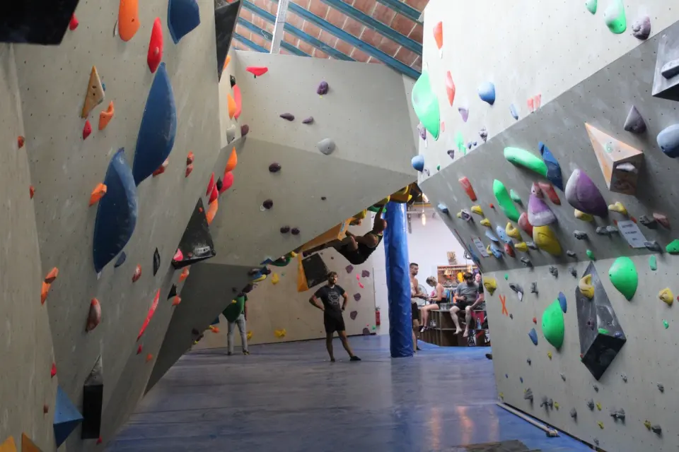 Climber on an overhang between steep walls covered in volumes, with others resting beyond