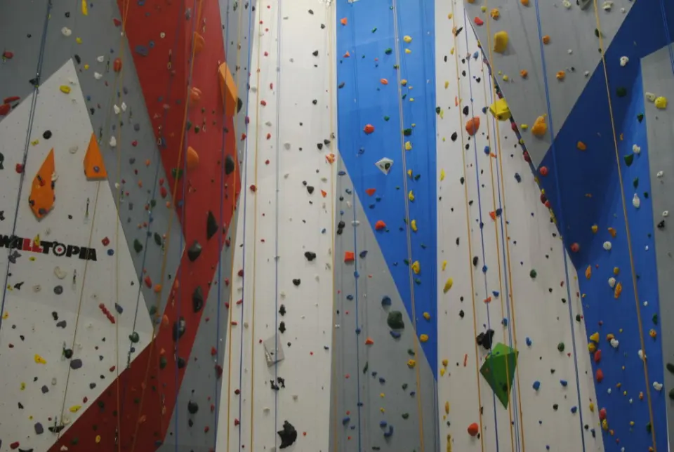 Tall roped walls in red, blue and grey with coloured holds and ropes hanging down