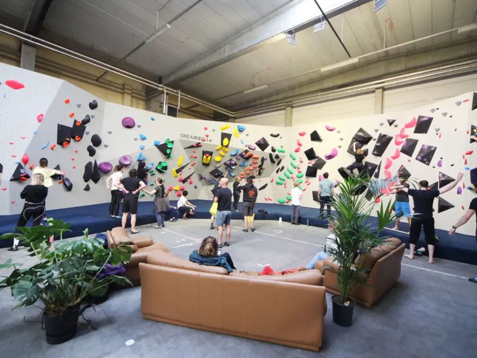 Climbers along the curved bouldering walls, with leather sofas and plants in the middle of the hall