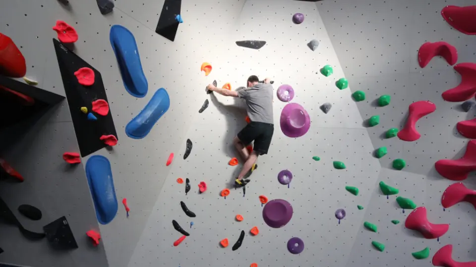 Climber on a grey wall with red, blue and purple holds