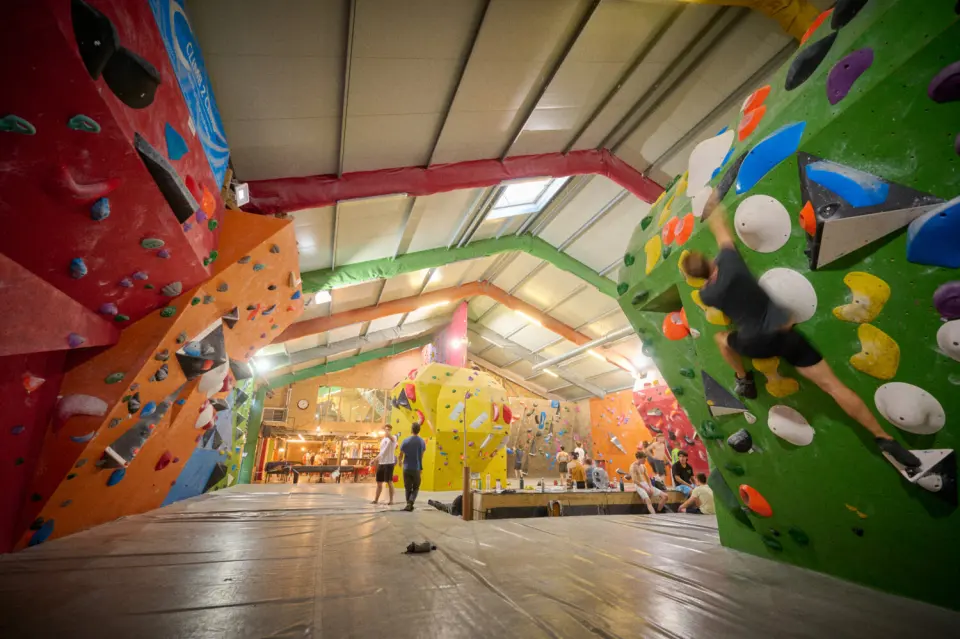 Boulderer on a green wall in the main hall, with colourful walls and the bar beyond