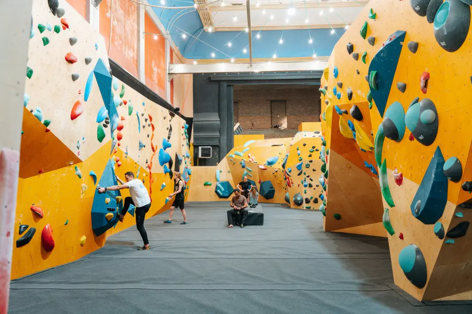 Yellow bouldering walls along both sides of the old theatre hall under a light-strung ceiling