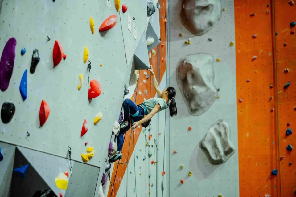 Climber leading up a steep grey wall with orange and grey walls behind