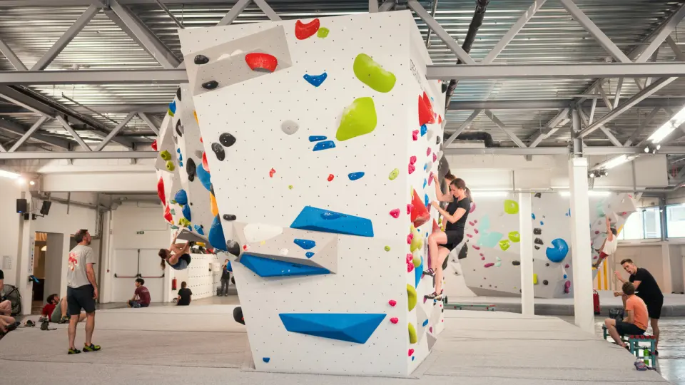 Climbers on a white freestanding boulder in the bright, steel-roofed bouldering hall