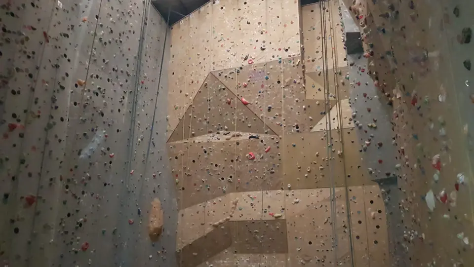Tall beige route walls with overhanging panels and ropes hanging down