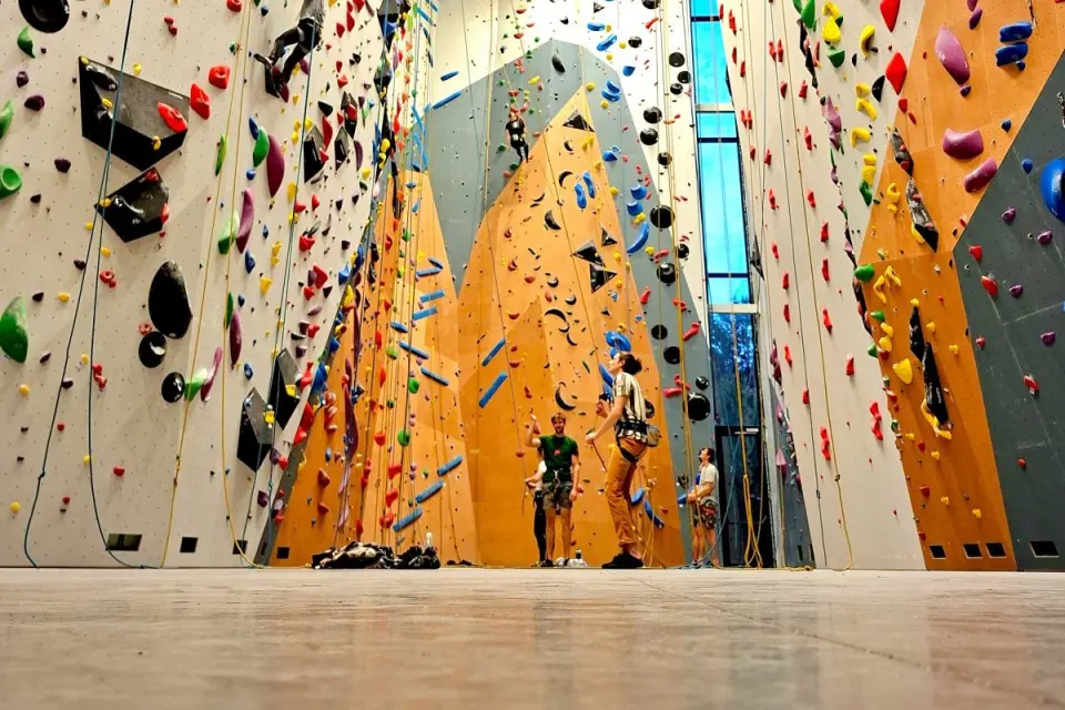 Climbers and belayers below the tall white, orange and grey rope walls