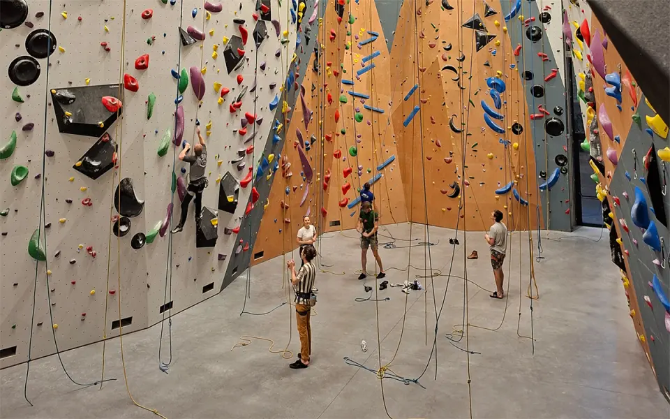 View over the rope hall with a climber on the grey wall and belayers on the floor