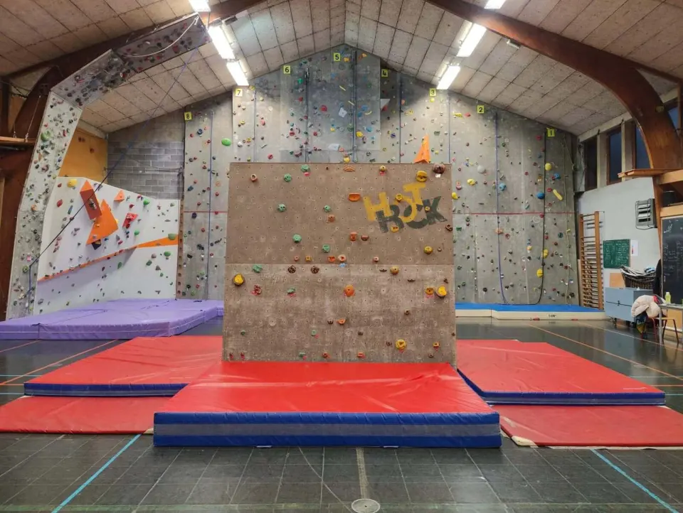 Freestanding bouldering block and mats in front of the numbered rope wall