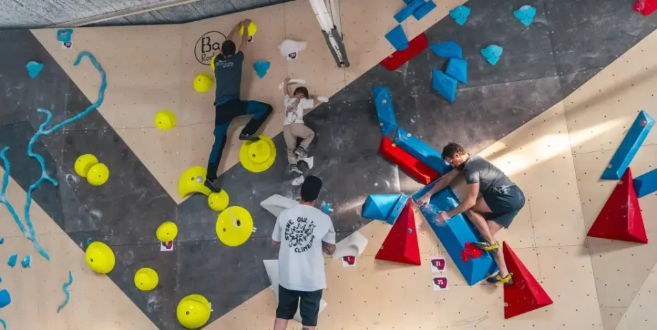 Climbers on a slab covered in yellow, blue and red volumes, seen from above