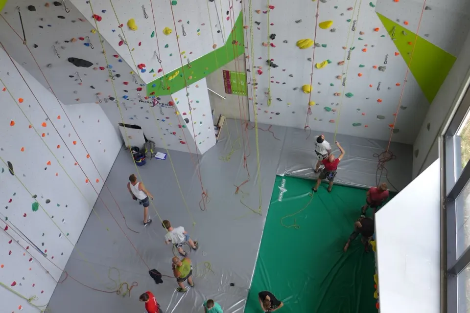 Climbers and belayers on the mats of the tall white rope hall, seen from above