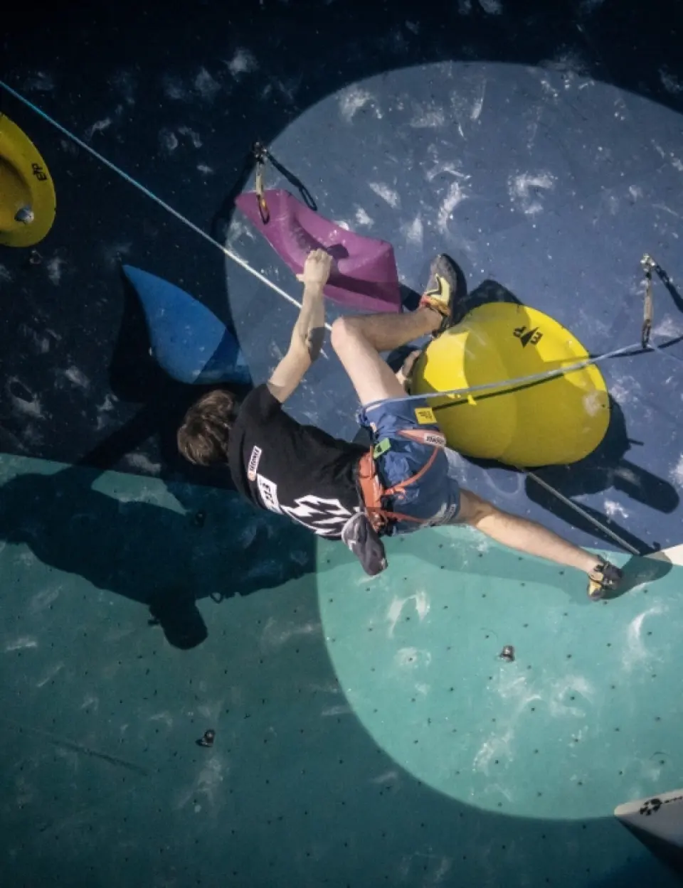 Lead climber clipping on an overhang with large yellow volumes, seen from above