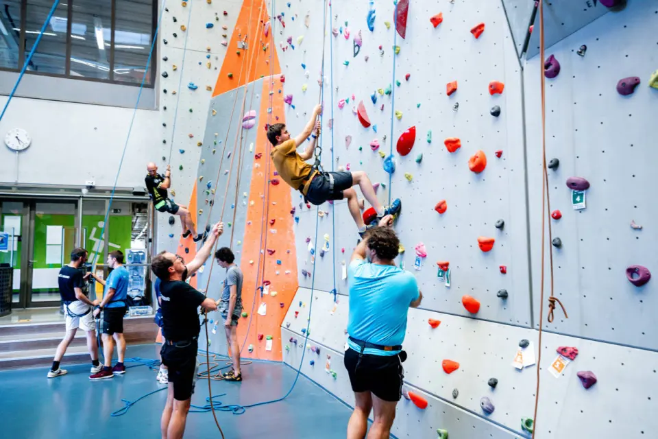 Climbers on top-rope with belayers on the floor of the grey and orange climbing hall