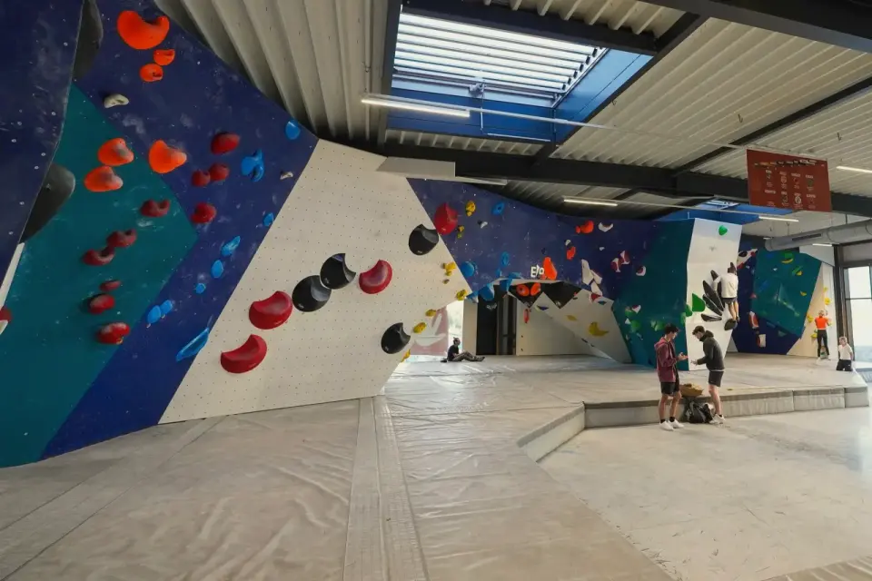 Blue, teal and white bouldering walls with matting under a glazed roof
