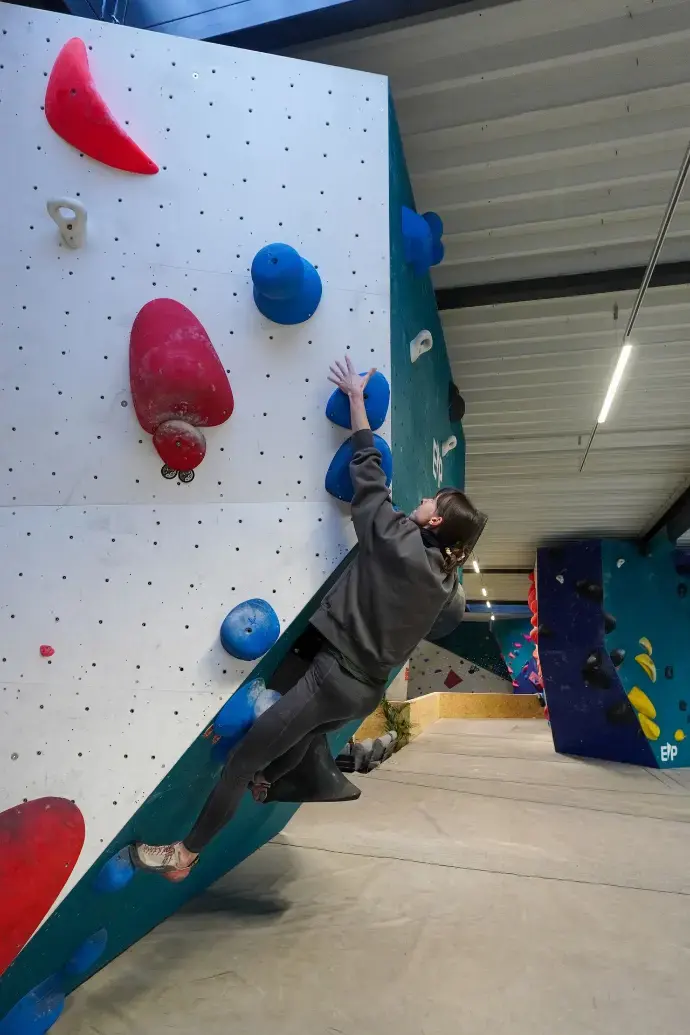 Climber reaching up an overhanging white boulder with big red and blue holds